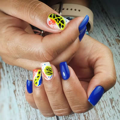 MANO UÑAS PINTADAS DE COLORES AZUL, AMARILLO Y BLANCO CON DISEÑOS ABSTRACTOS